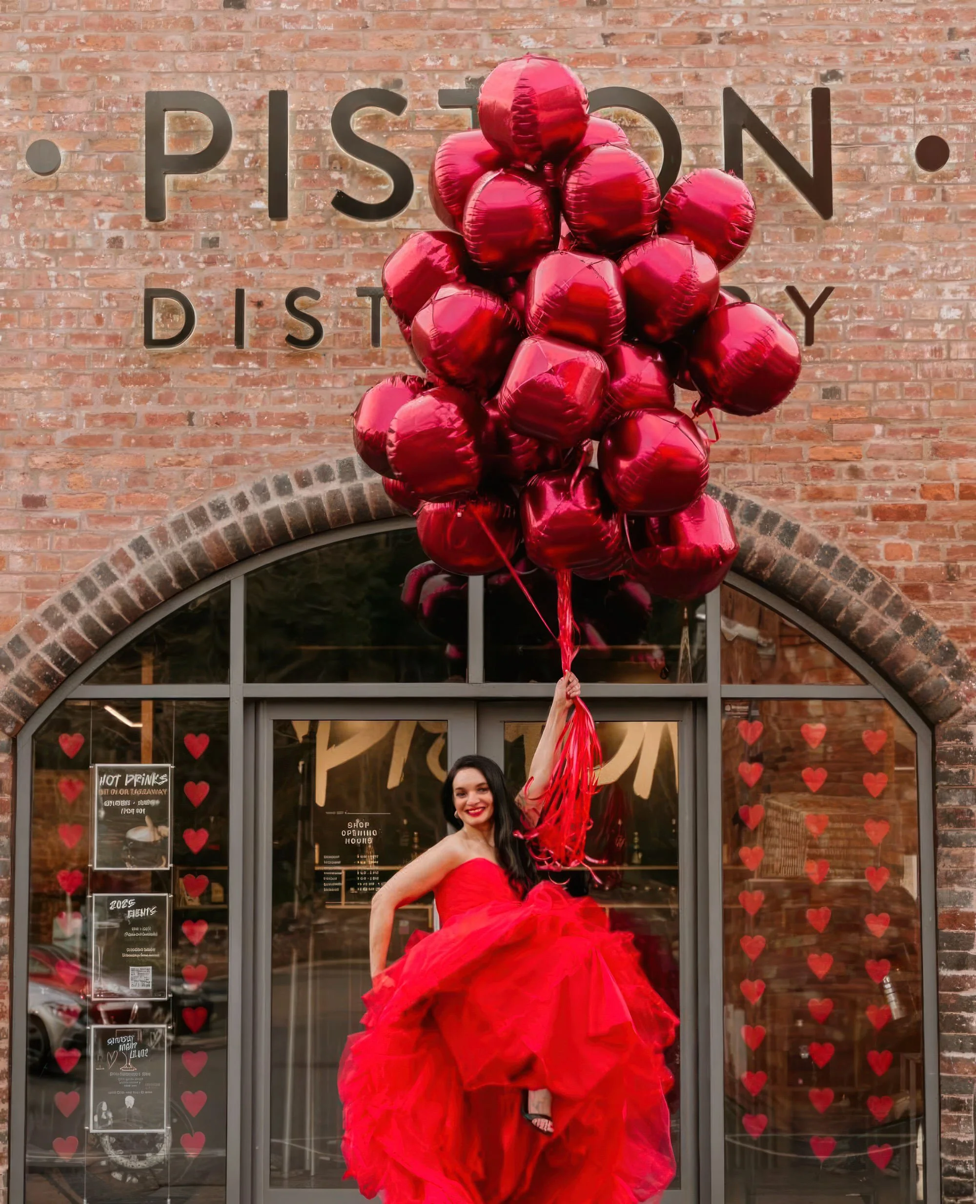 Bride in red ballgown holding red heart balloons outside Piston Distillery, wedding decor hire Worcestershire