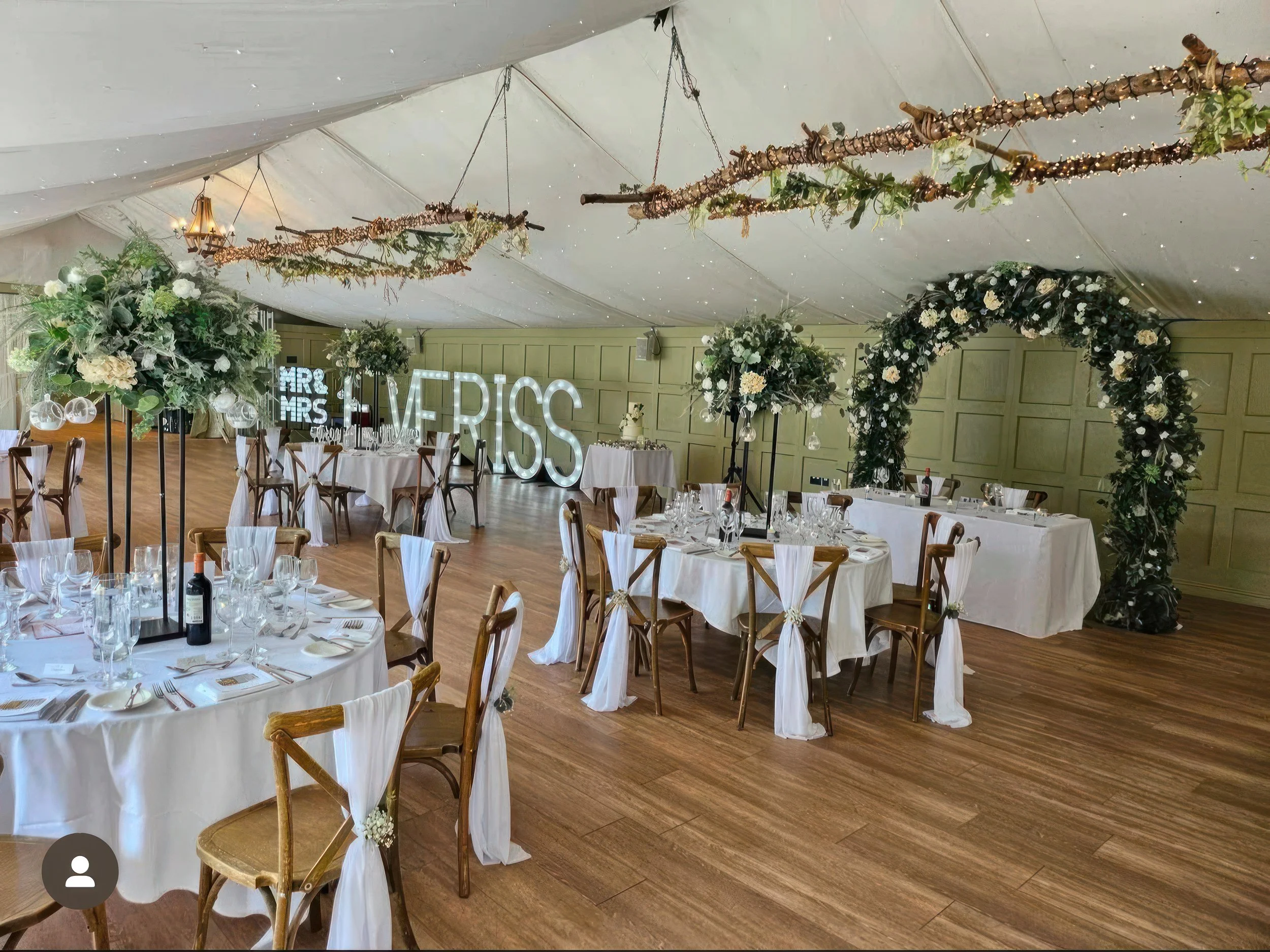 Wedding decor hire Hogarths Hotel Solihull — illuminated surname letters, floral wedding arch, tall table centrepieces with greenery, rustic ceiling decor, cross-back chairs with white sashes