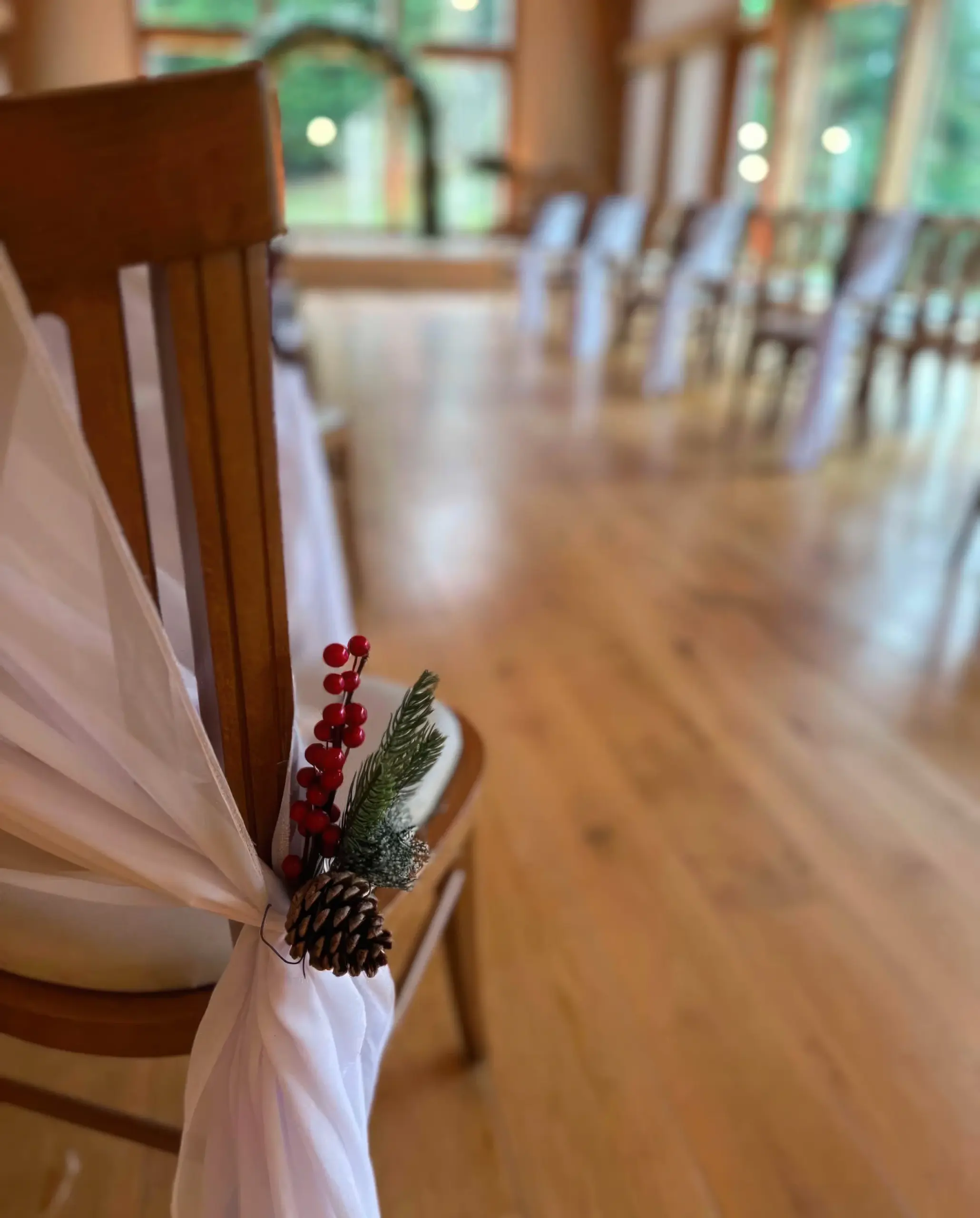 wedding aisle decor Mill Barns Worcestershire — white chair sash with winter pine cone and red berry detail by The Wedding House
