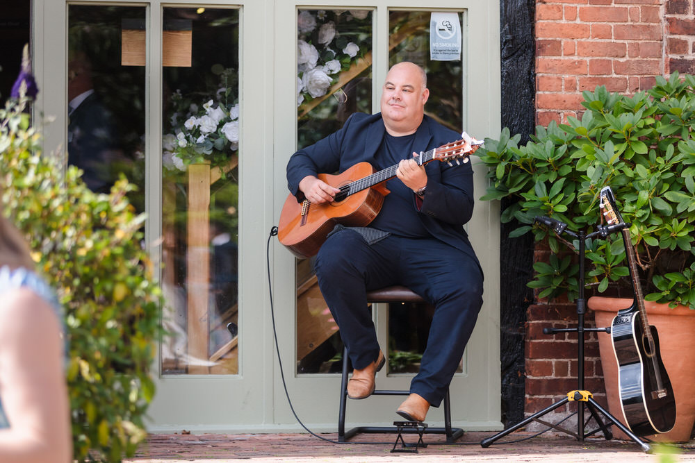 Wedding guitarist Stuart Toogood performing acoustic guitar at outdoor drinks reception at Curradine Barns Worcestershire