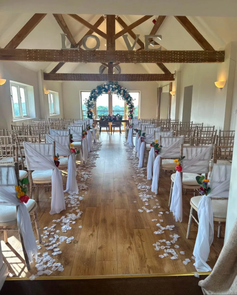 Wedding ceremony aisle decor at Bordesley Park with white chair drapes, petals on aisle and floral arch backdrop