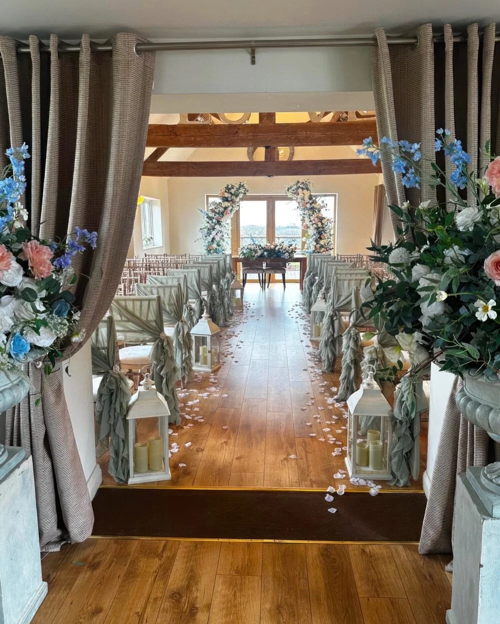 Wedding ceremony aisle at Bordesley Park with sage green chair drapes, lanterns, petals and floral entrance styling
