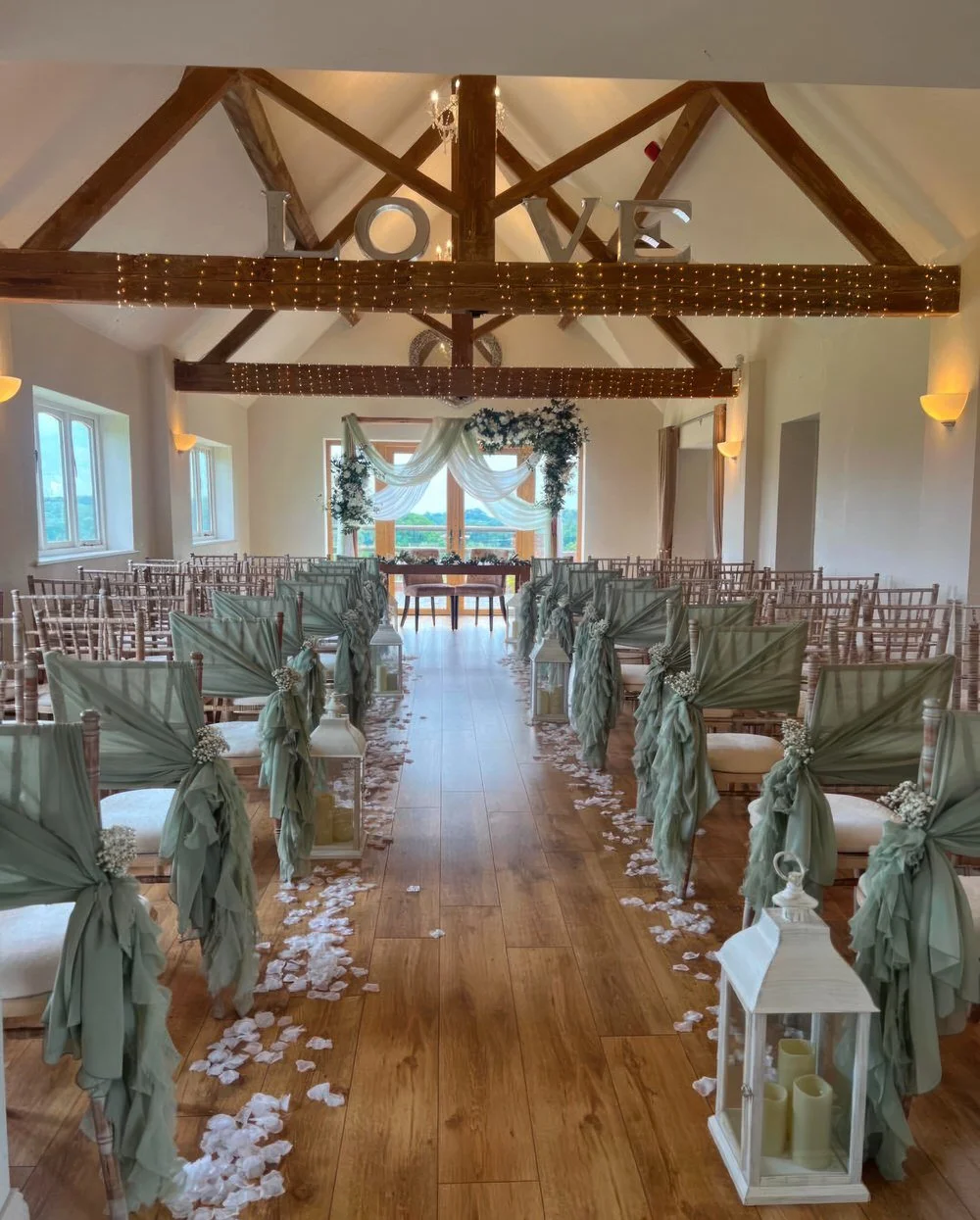 Sage green wedding ceremony decor at Bordesley Park with draped chair sashes, aisle petals and lanterns