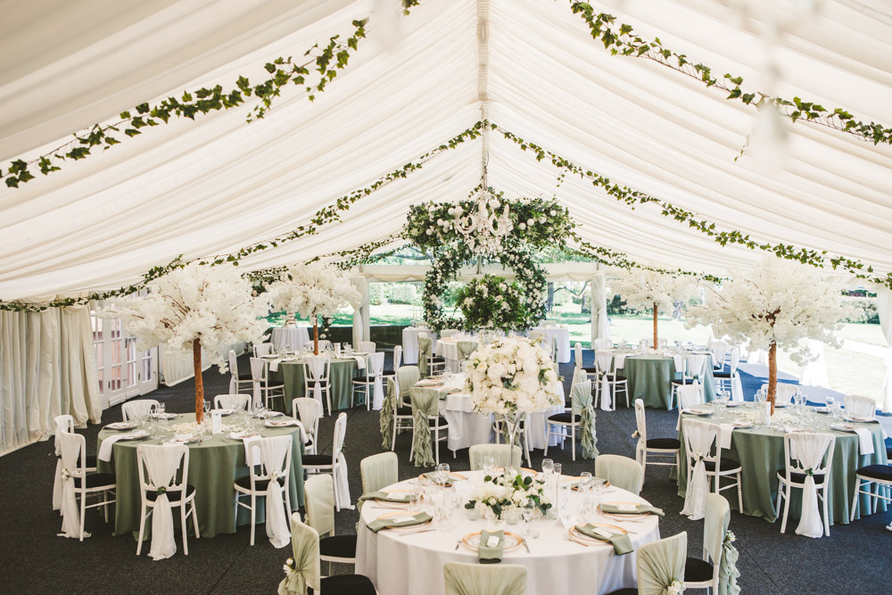 Wedding reception marquee decor at Bordesley Park with sage green table styling, centrepieces and ceiling greenery