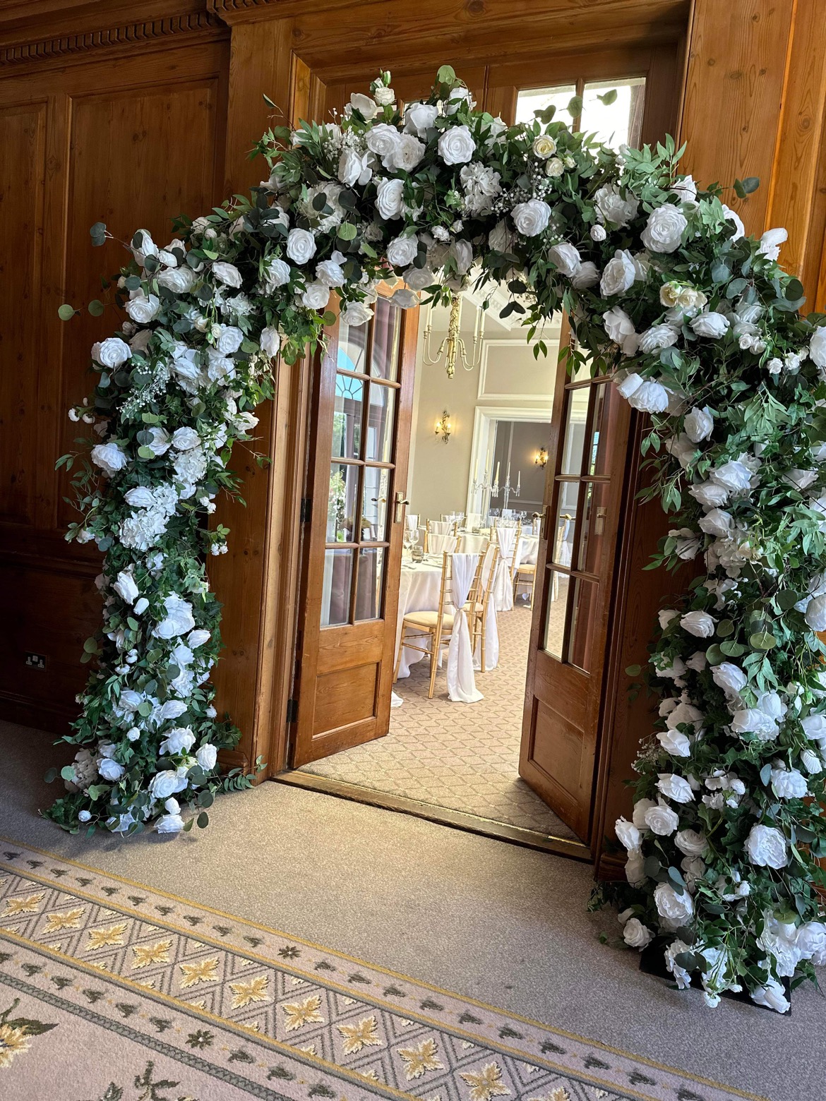 wedding arch with white and green artificial flowers at Brockencote Hall doorway leading into reception room