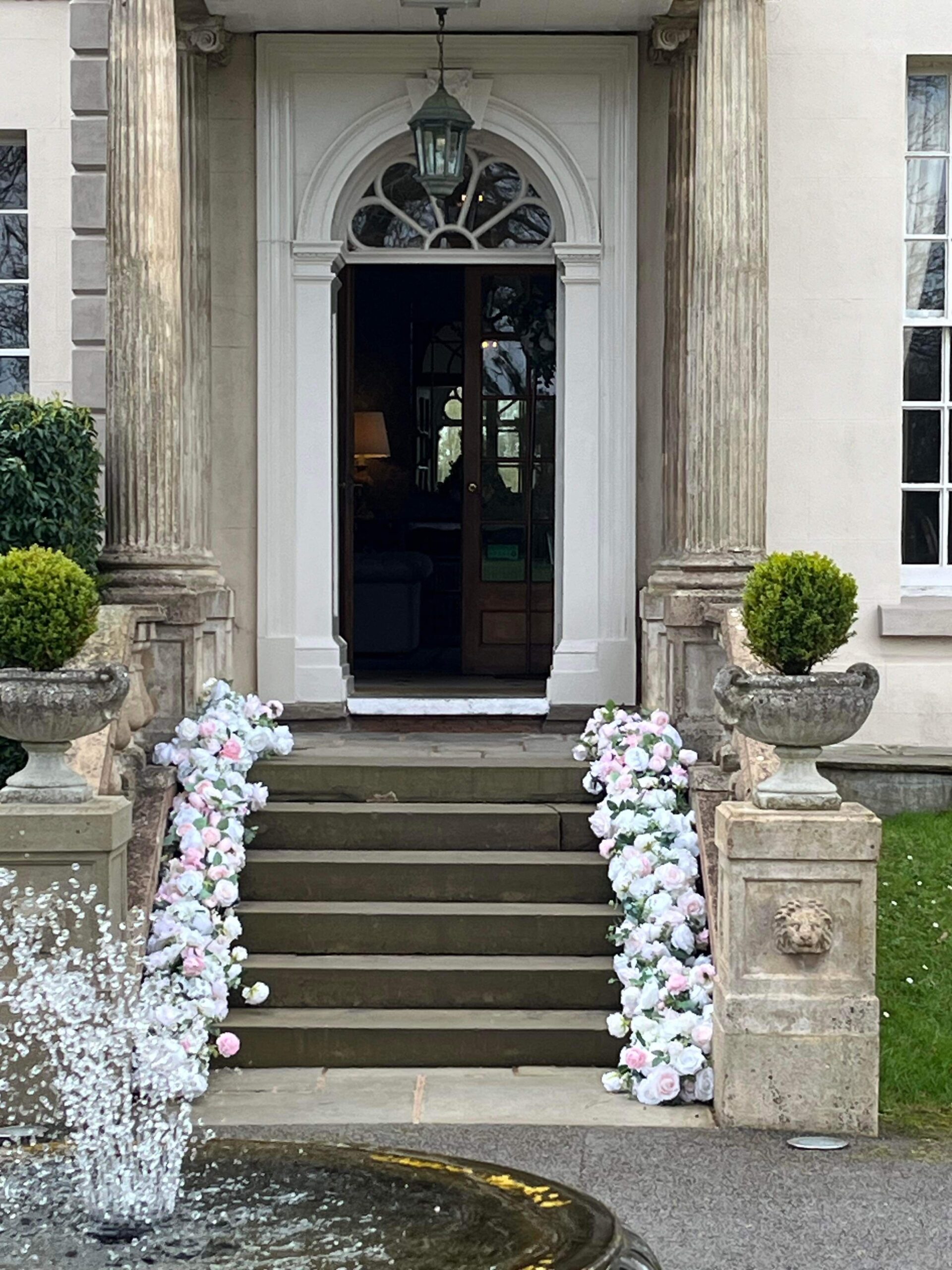 Brockencote Hall wedding entrance with floral staircase decor, pastel artificial flowers and elegant country house doorway