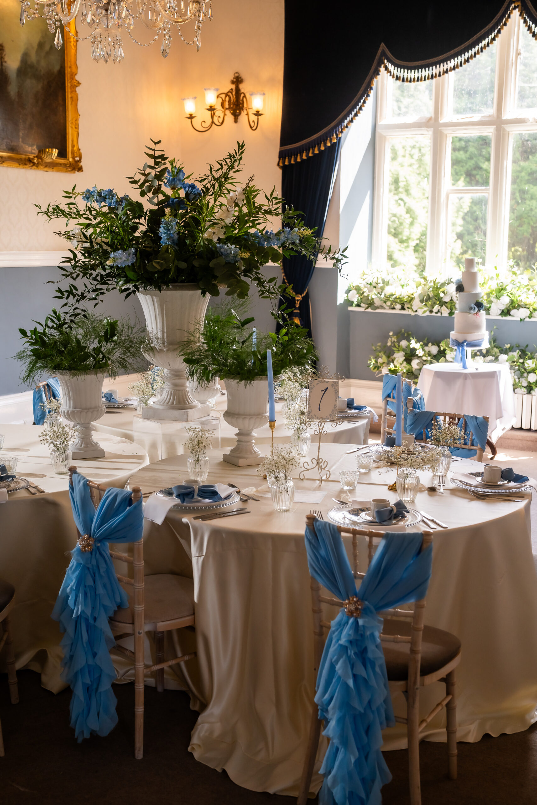 Round wedding tables with blue chair decor, urn floral centrepieces and candles in Great Parlour at Grafton Manor wedding decor hire Worcestershire