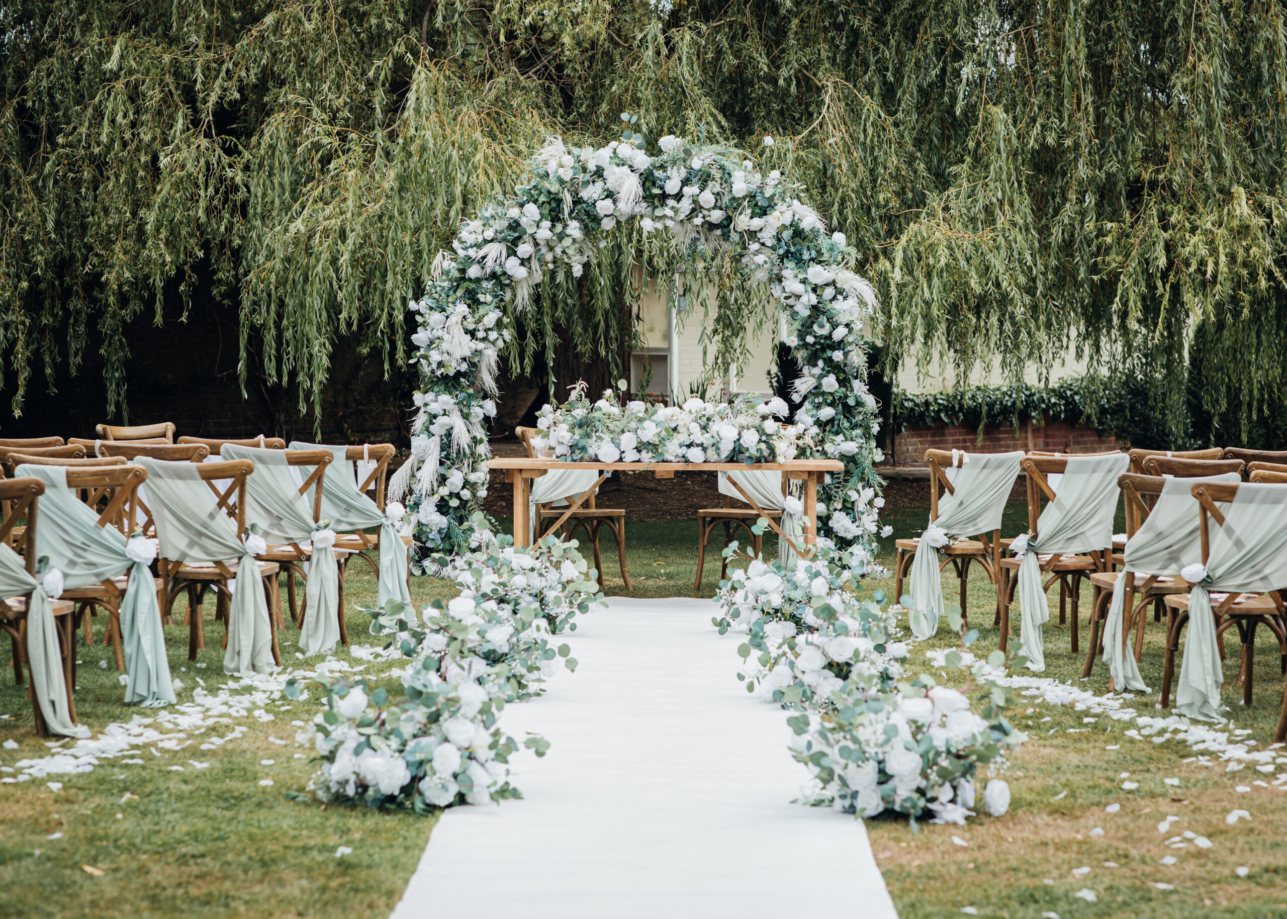 Hogarths Stone Manor outdoor wedding ceremony with floral arch, white aisle runner, eucalyptus arrangements and sage green chair drapes