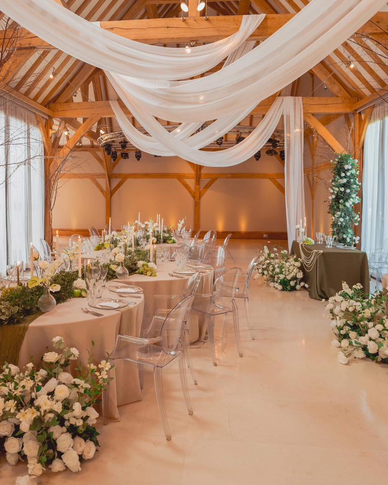 Wedding decor hire at Redhouse Barn with ceiling draping, round tables, floral arrangements and styled cake table area