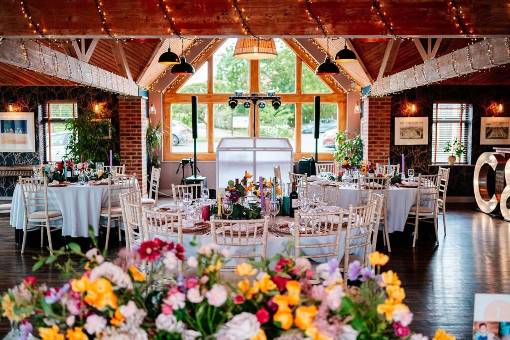 Rustic wedding reception decor with round tables, colourful floral centrepieces, chiavari chairs and LOVE letters inside a barn style wedding venue