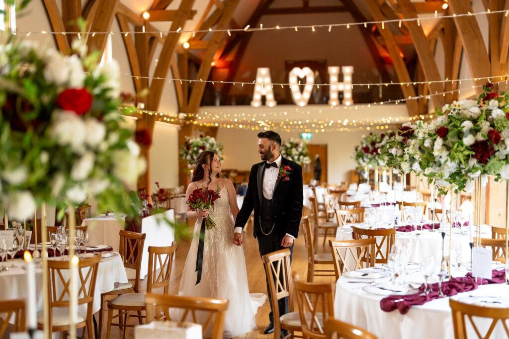 Bride and groom walking through wedding reception at The Mill Barns with floral centrepieces and fairy lights