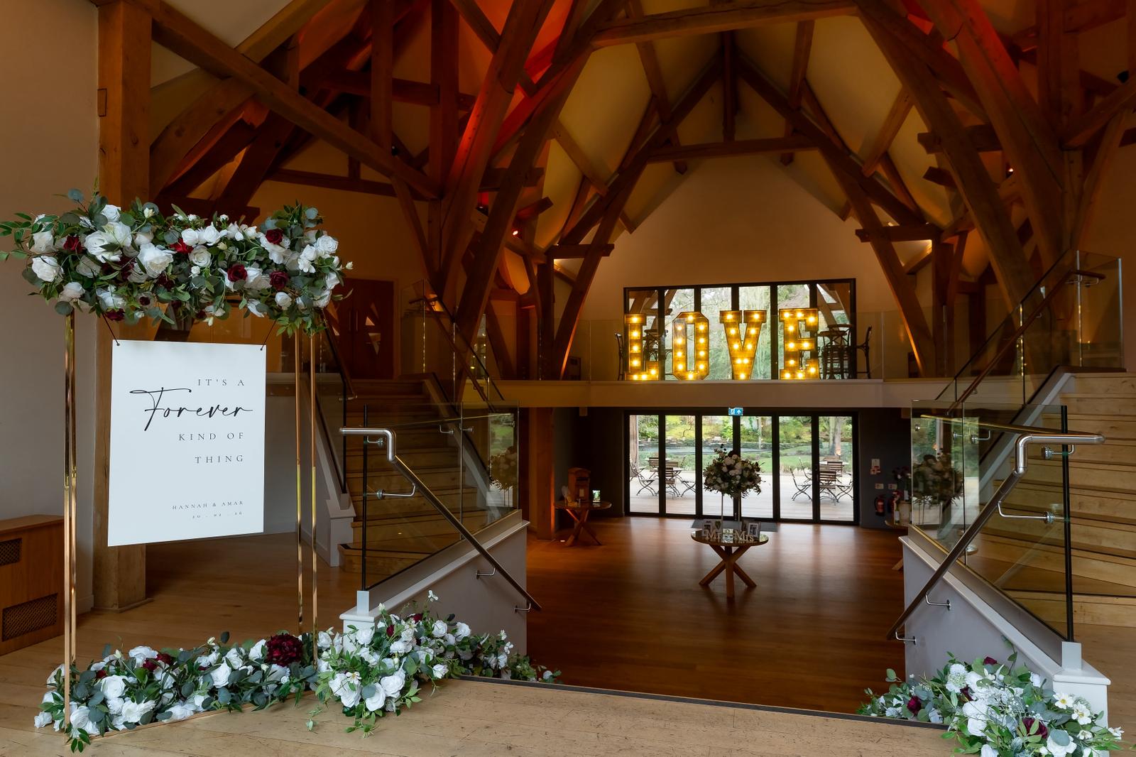Wedding venue entrance styling at The Mill Barns with welcome sign, floral arrangements and illuminated LOVE letters
