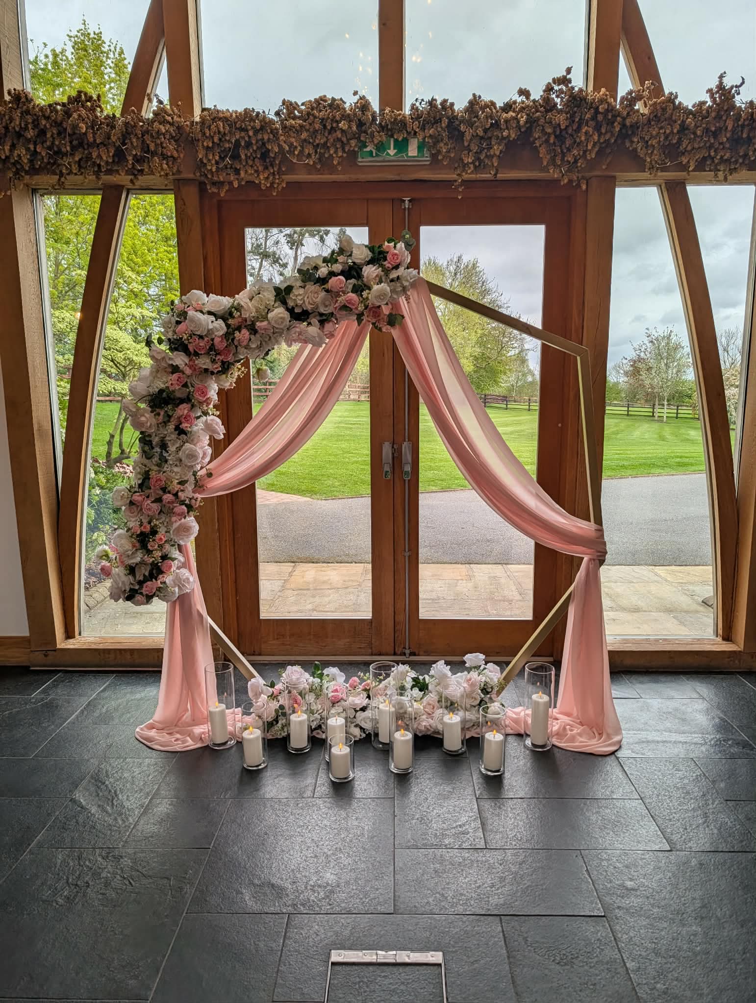 Hexagon wedding arch with pink draping and floral arrangement at Mythe Barn ceremony