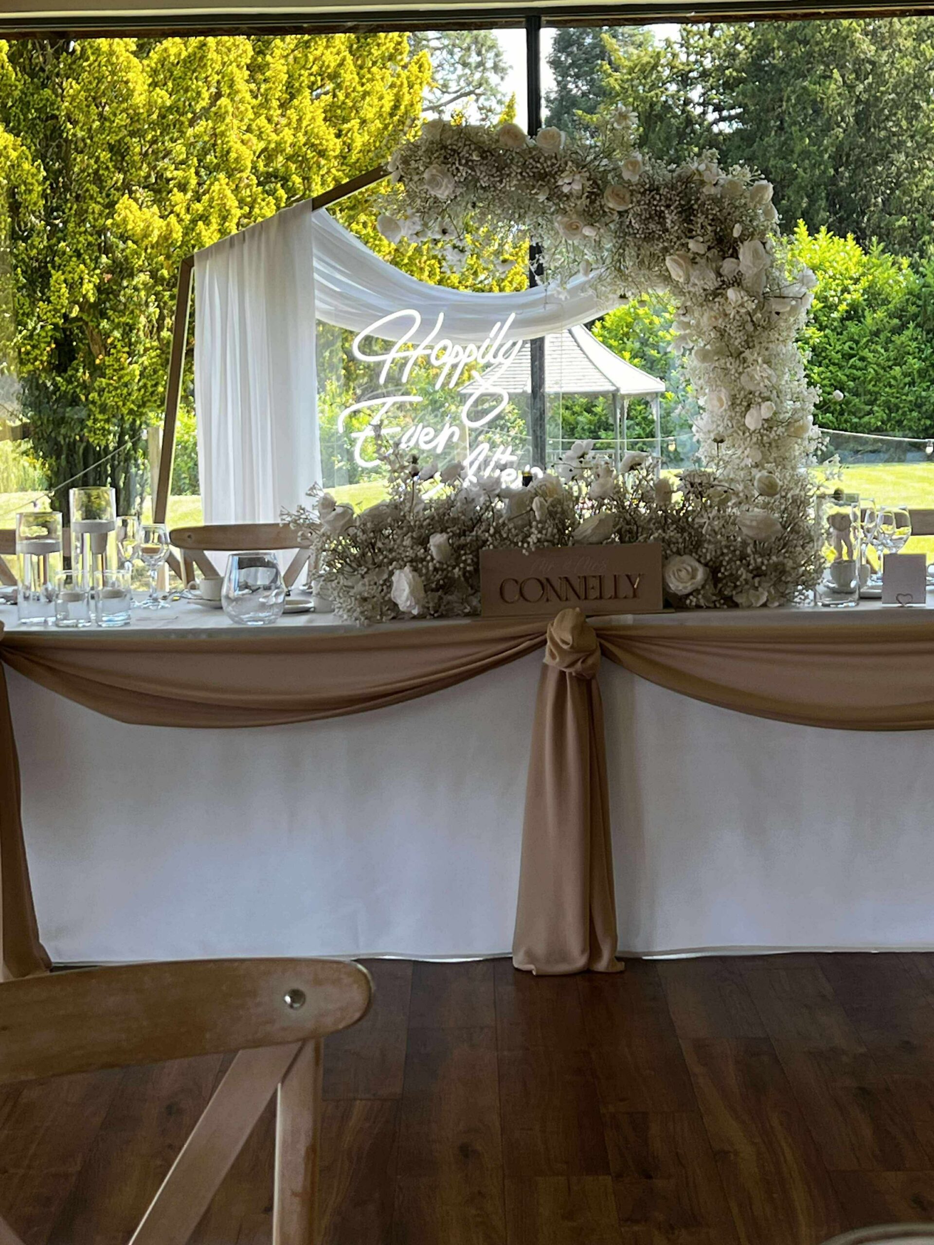 Champagne draped top table with white floral arrangement and Happily Ever After neon sign at Bredenbury Court Barns wedding