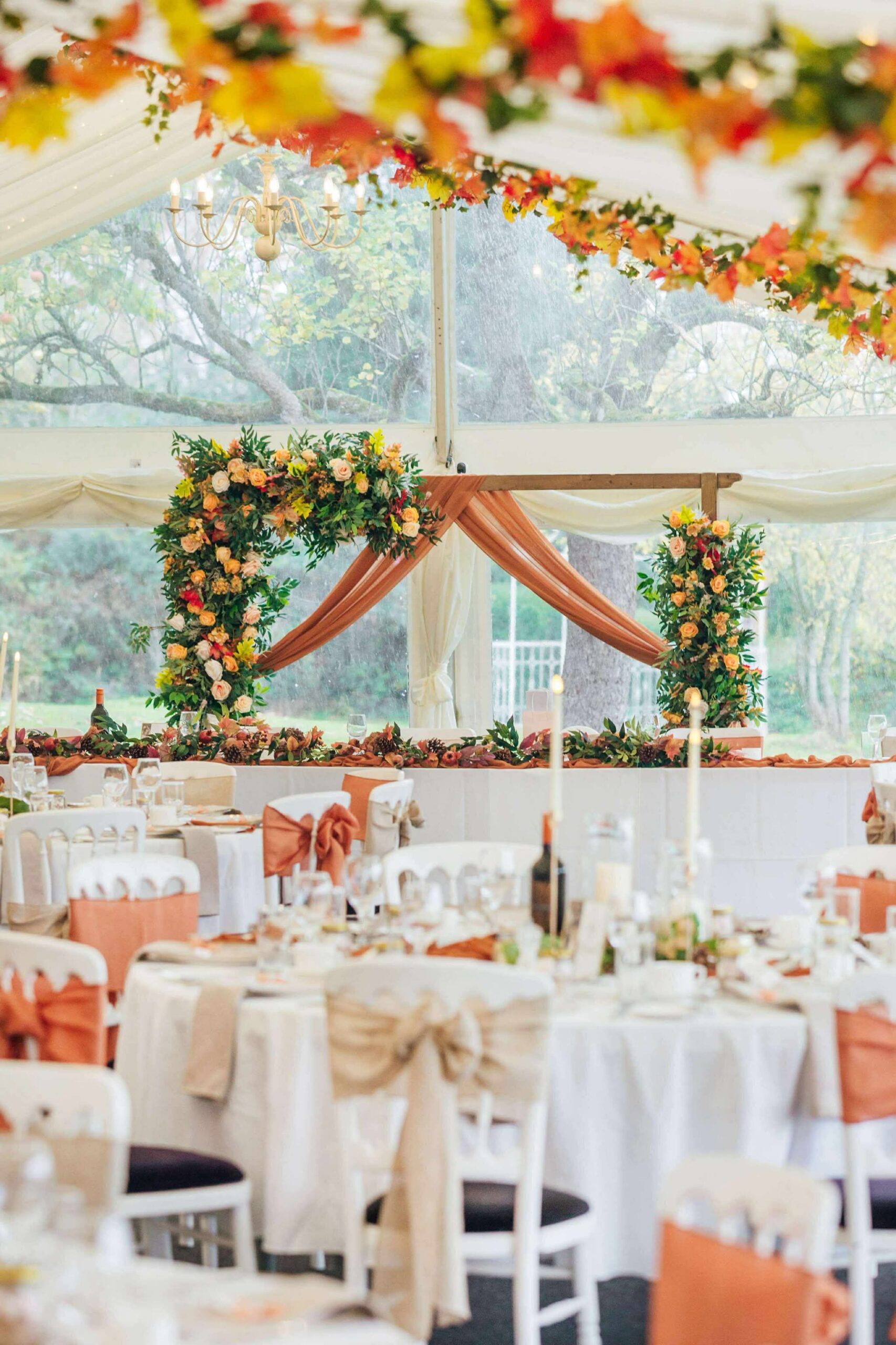 Rust and champagne wedding decor with draped arch, autumn floral garland and candlelit top table inside marquee at Bordesley Park