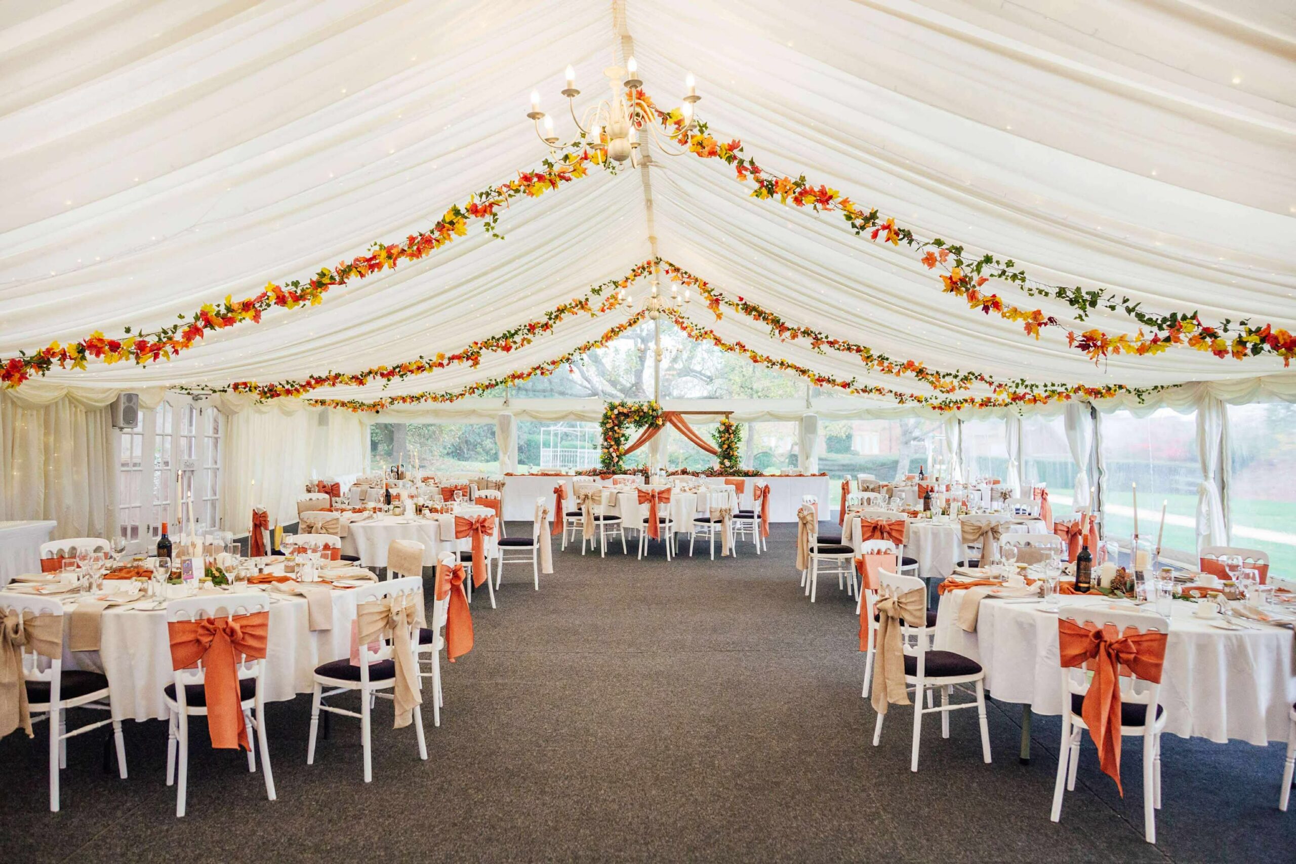 Marquee wedding decor with autumn ceiling foliage, rust and champagne chair decor and styled tables at Bordesley Park