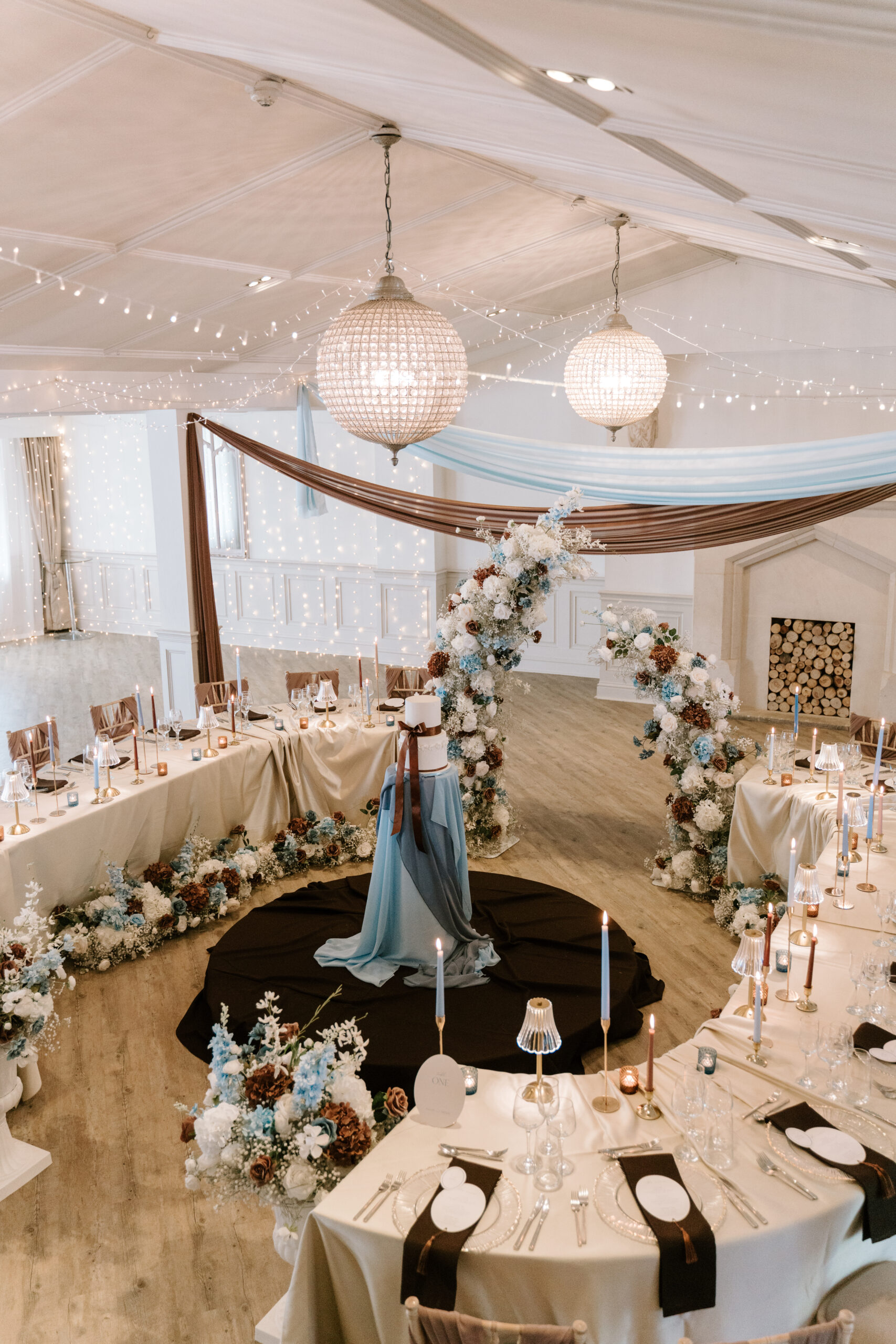 Blue and brown wedding decor with serpentine tables, draped ceiling and central cake display at Manor By The Lake