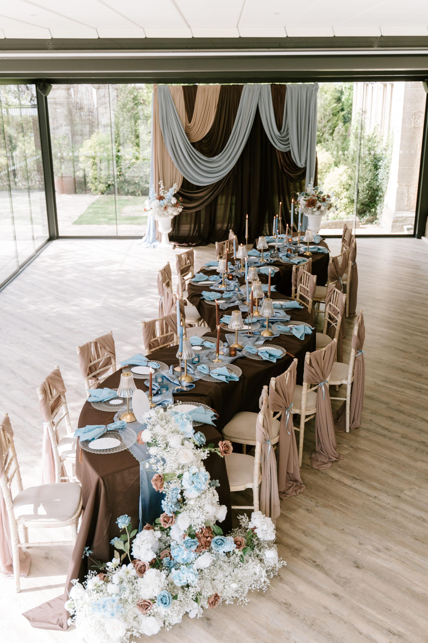 Serpentine wedding table with chocolate linen, blue napkins and floral runner at Manor By The Lake