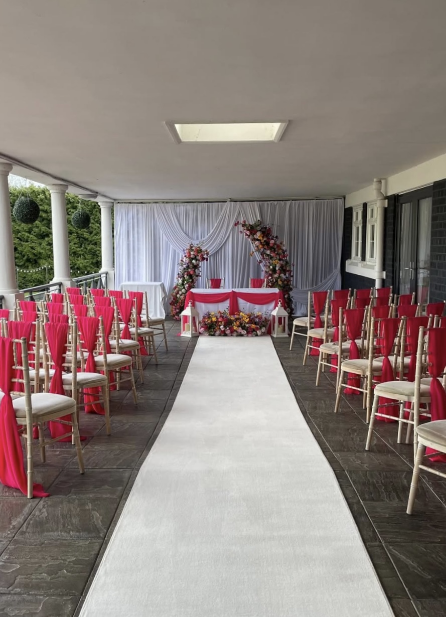 Wedding ceremony aisle with white runner pink chair drapes and floral backdrop at The Holt Fleet