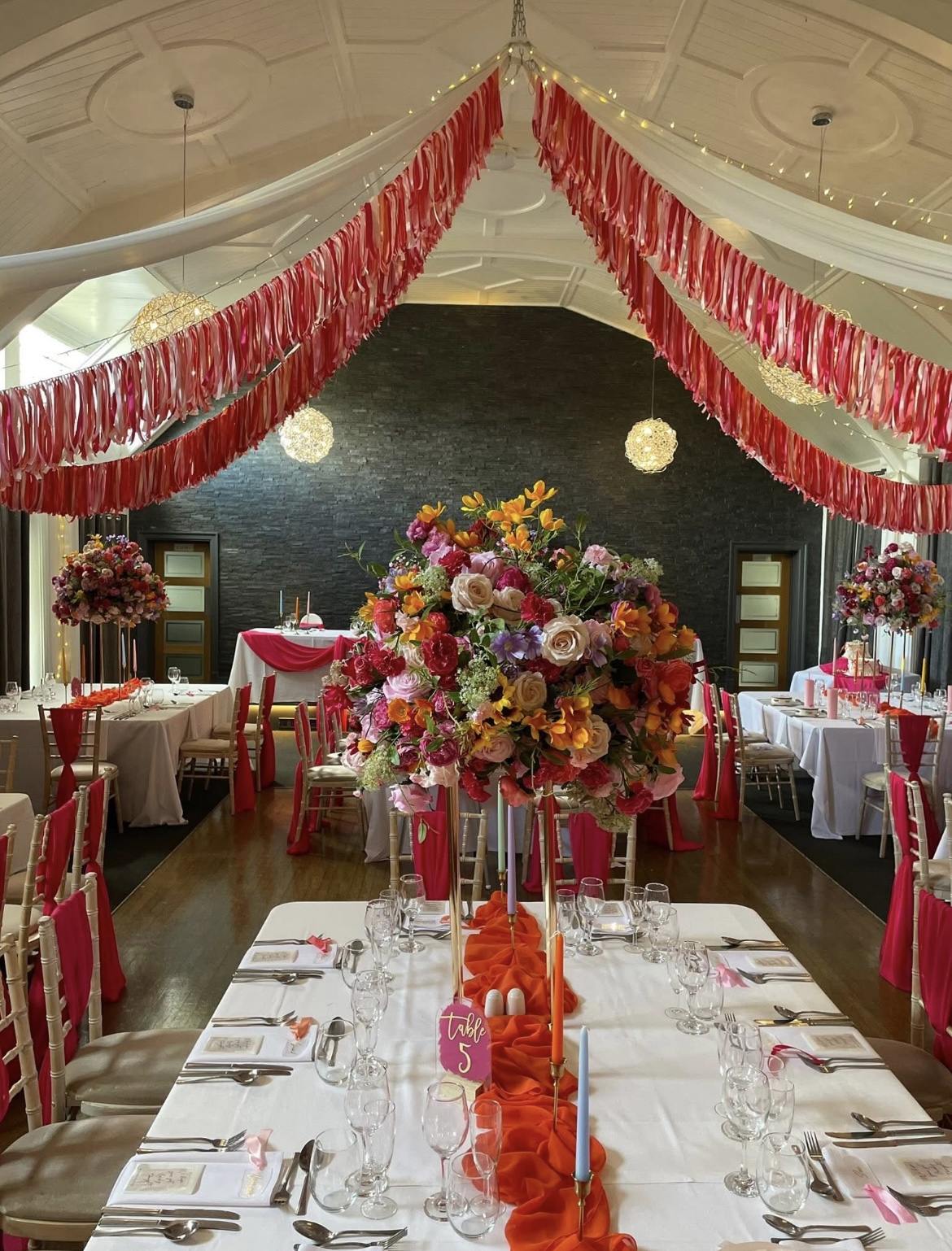 Pink and orange wedding reception decor with tall floral centrepieces and ribbon ceiling at The Holt Fleet