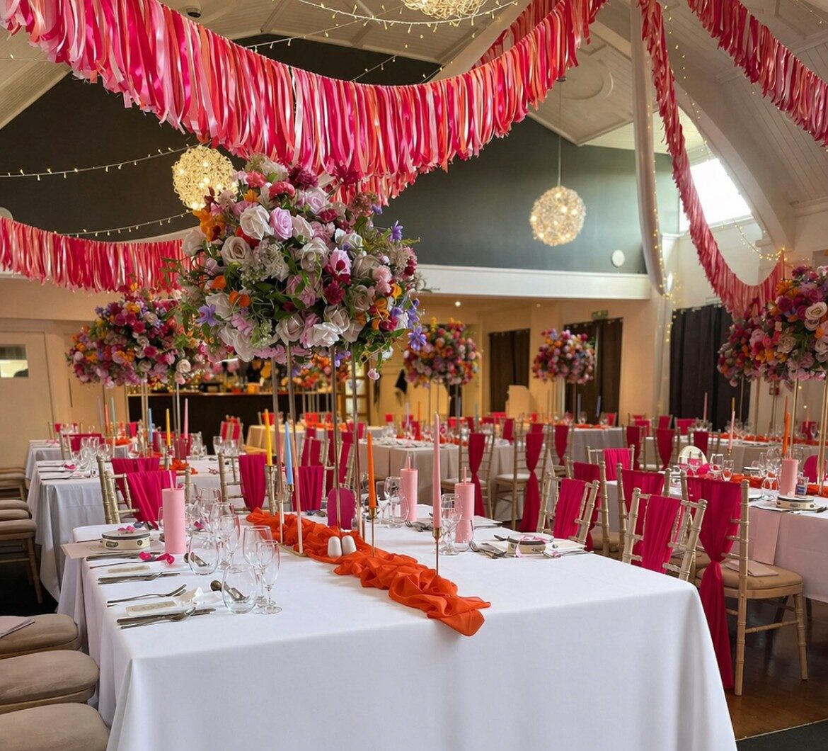Pink and orange wedding reception decor with tall floral centrepieces and ribbon ceiling at The Holt Fleet