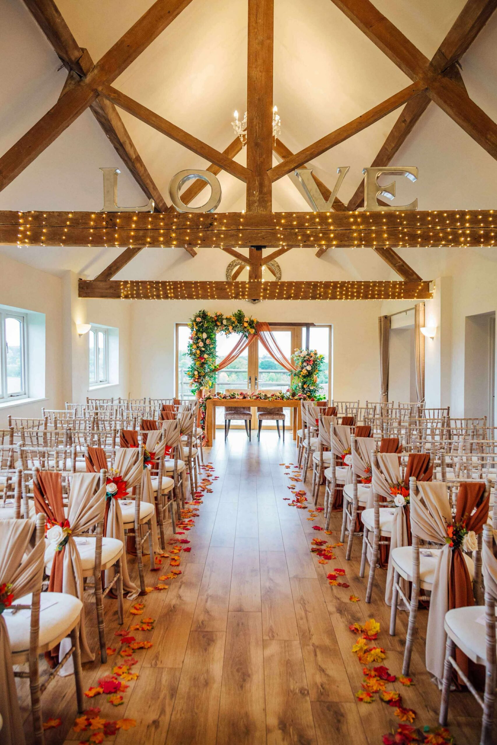 Autumn wedding ceremony aisle with rust and champagne chair decor, petal aisle and draped arch backdrop at Bordesley Park