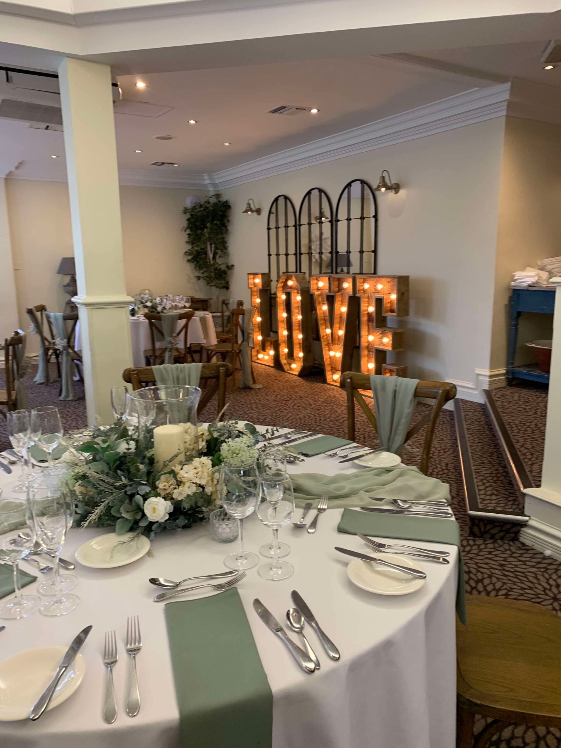 Sage green wedding table decor with foliage centrepiece and rustic LOVE letters at Stone Manor Hotel